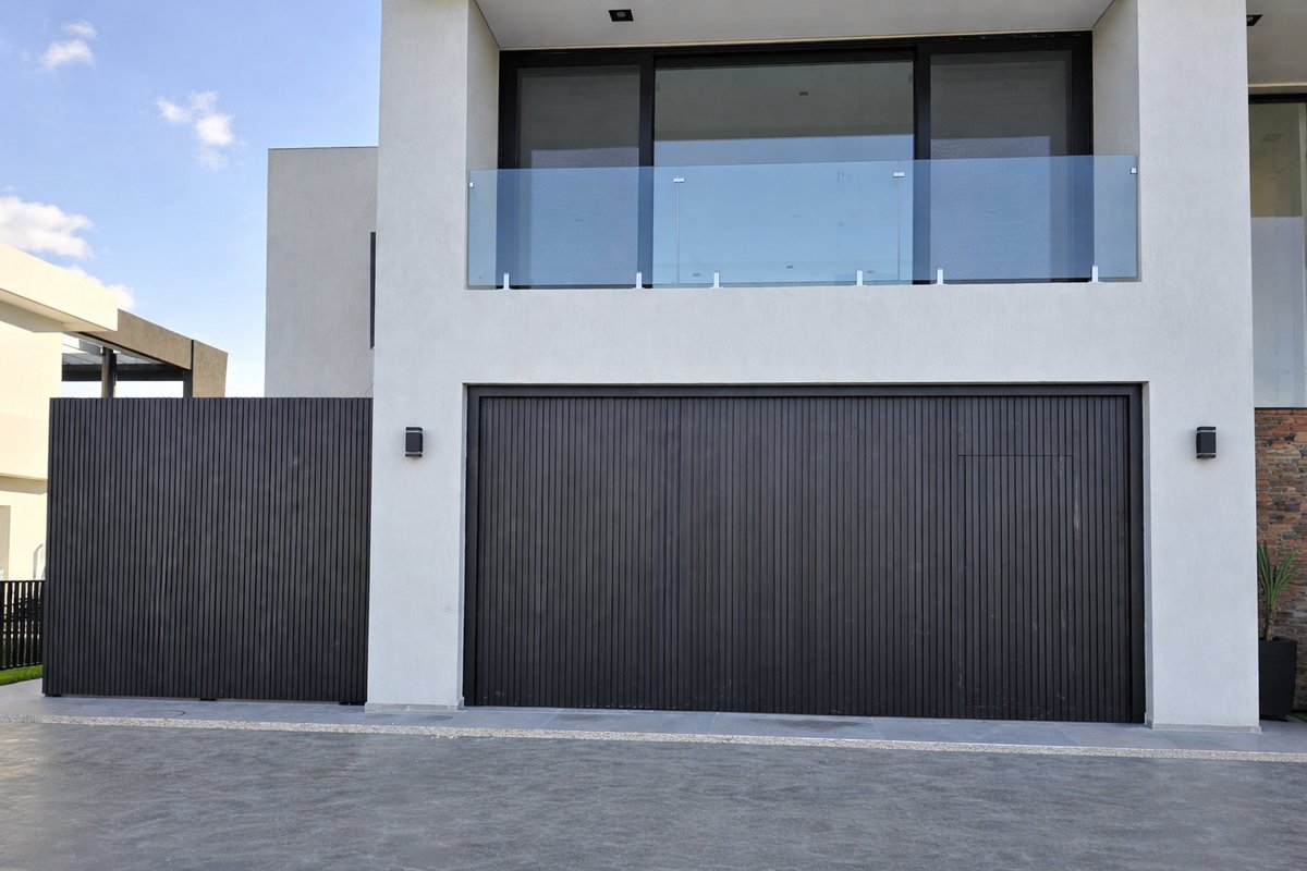 Portón corredizo de hierro con tablillas verticales en frente de vivienda moderna